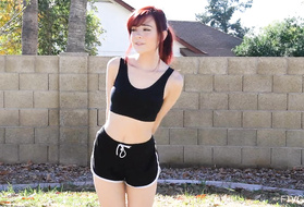 Рыжая девушка занимается голышом спортивной разминкой во дворе